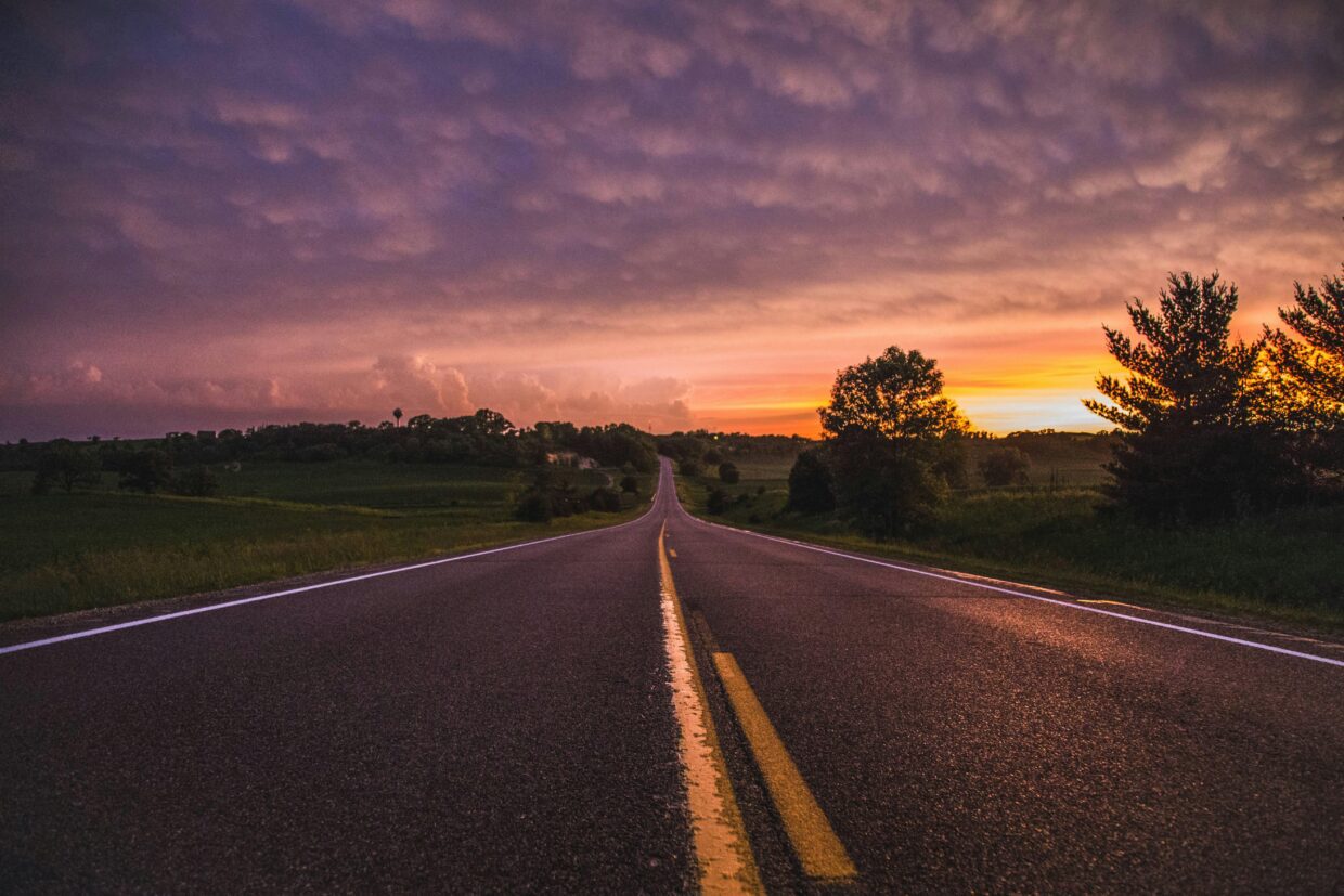Estrada de asfalto reta ao pôr do sol sob céu roxo e alaranjado