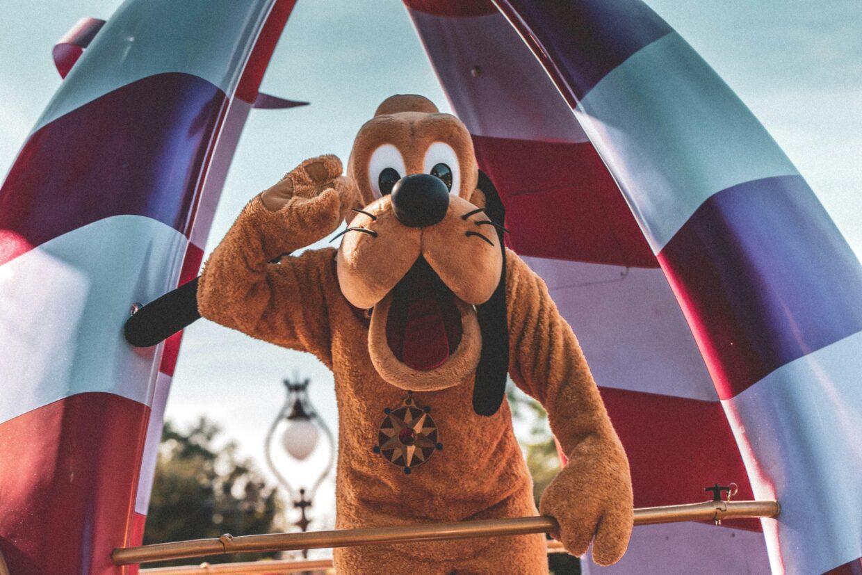 Personagem Pluto fantasiado em frente a uma tenda listrada vermelha e branca, na Disney