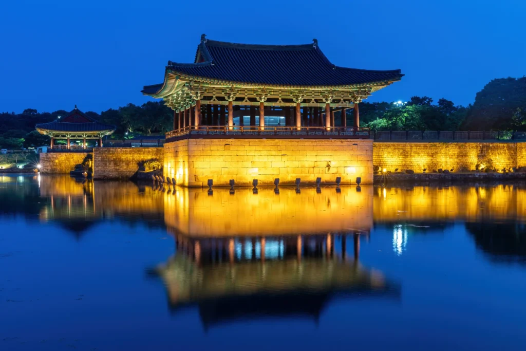 Pavilhão iluminado de Donggung refletido nas águas do lago Wolji ao anoitecer, em Gyeongju.