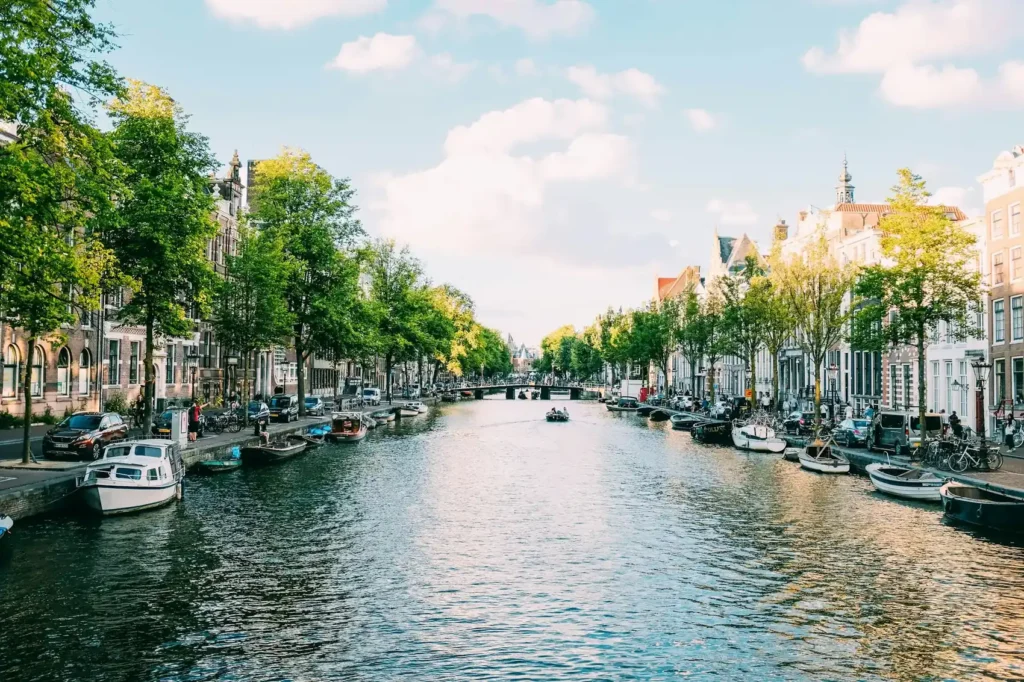 Canal de Amsterdam com barcos e árvores à beira da água