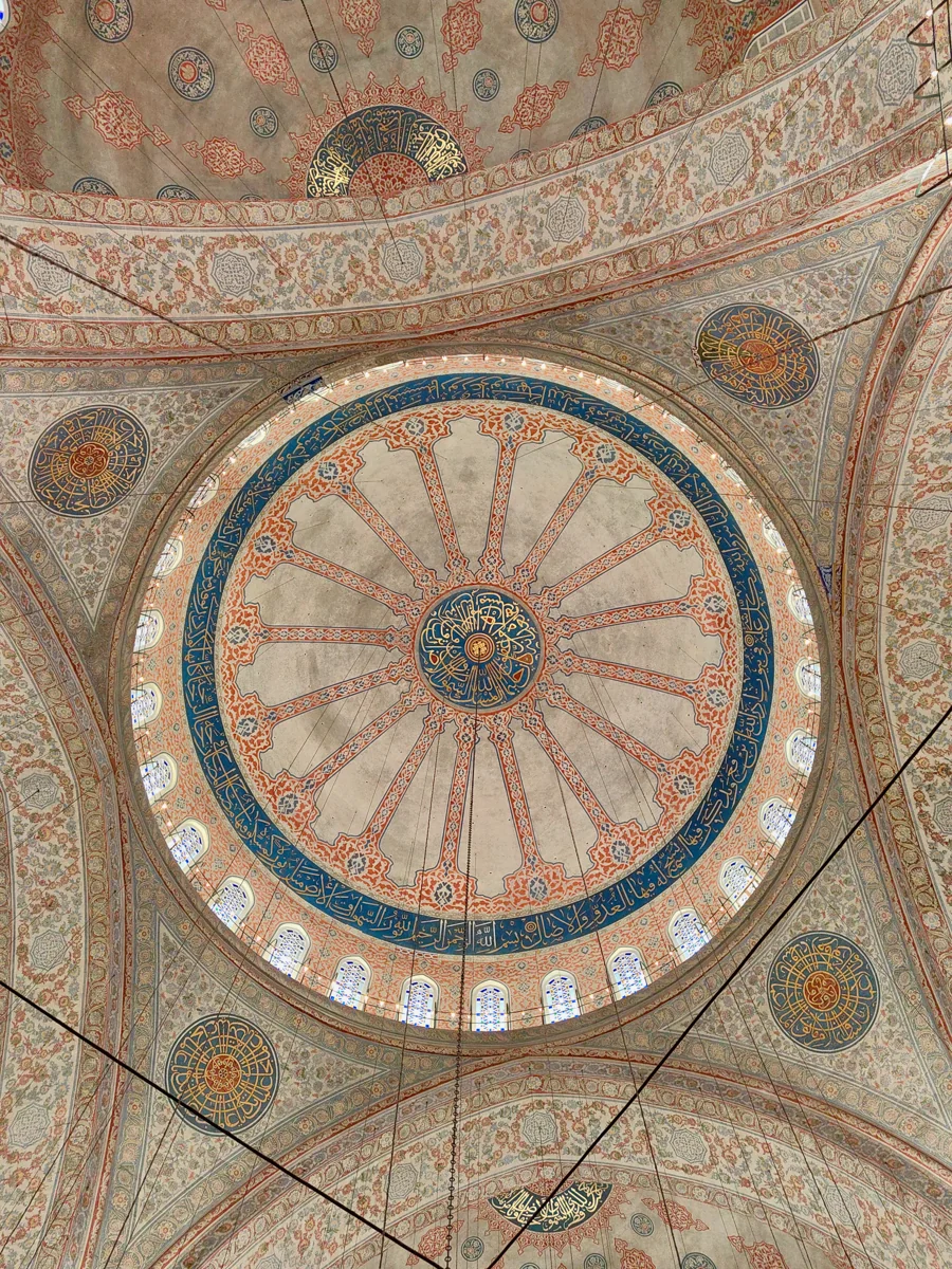 Cúpula e arcos decorados no interior da Mesquita Azul, em Istambul, com motivos florais e inscrições.