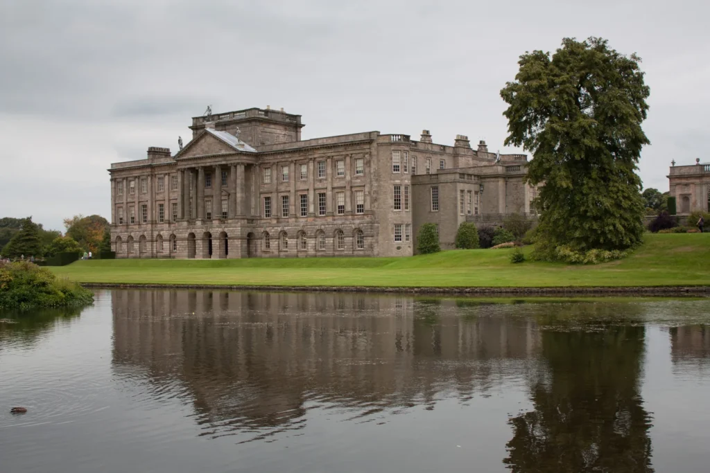 Casa de Lyme Park refletida no lago, com gramado e árvores ao redor.