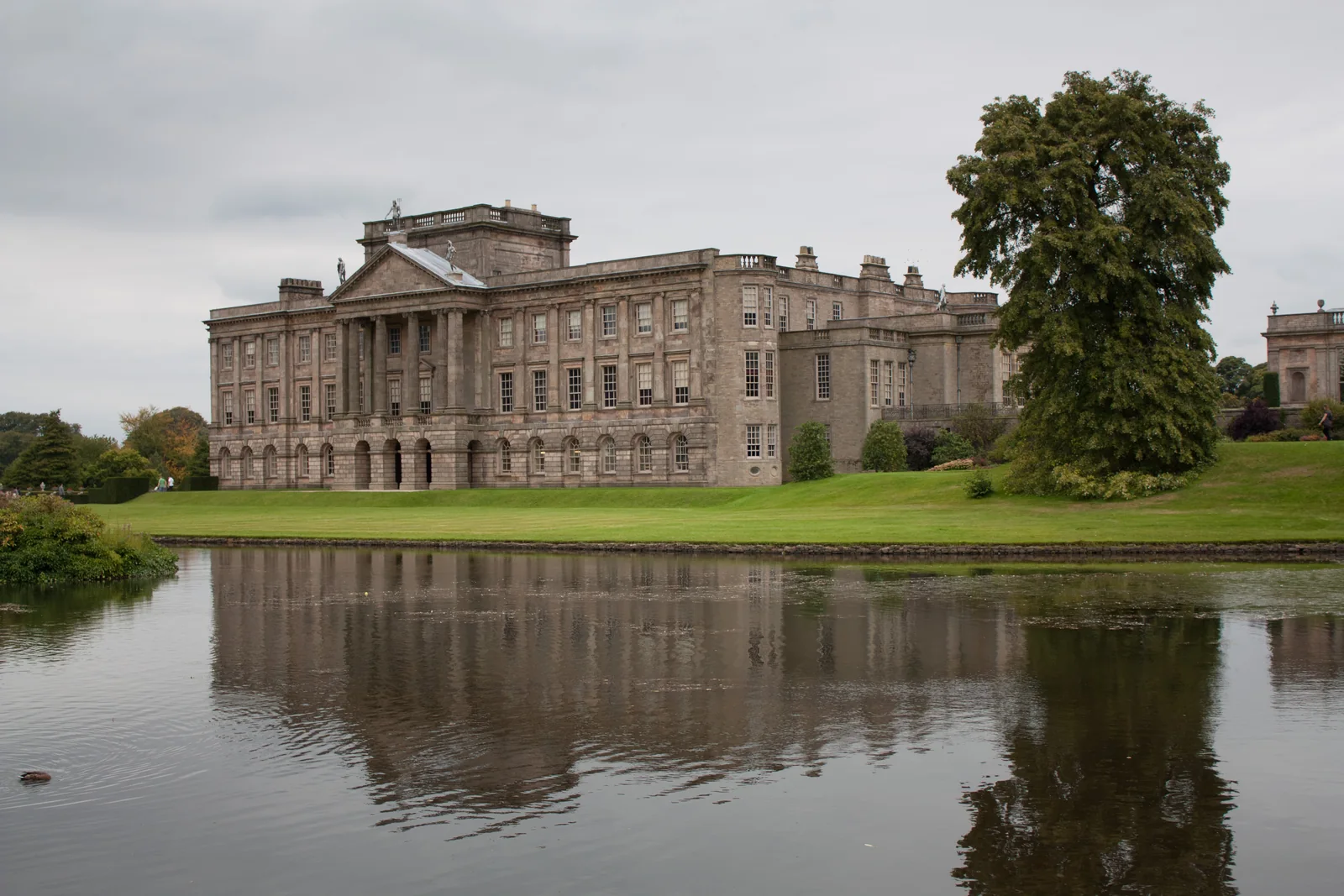 Casa de Lyme Park refletida no lago, com gramado e árvores ao redor.