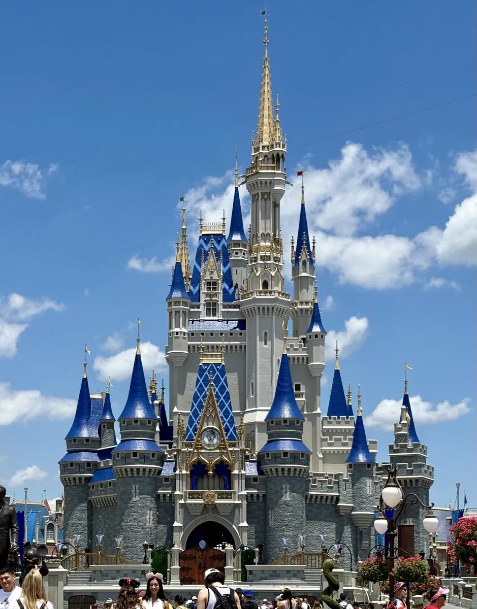 Castelo da Cinderela no Magic Kingdom, com torres azuis sob um céu ensolarado.