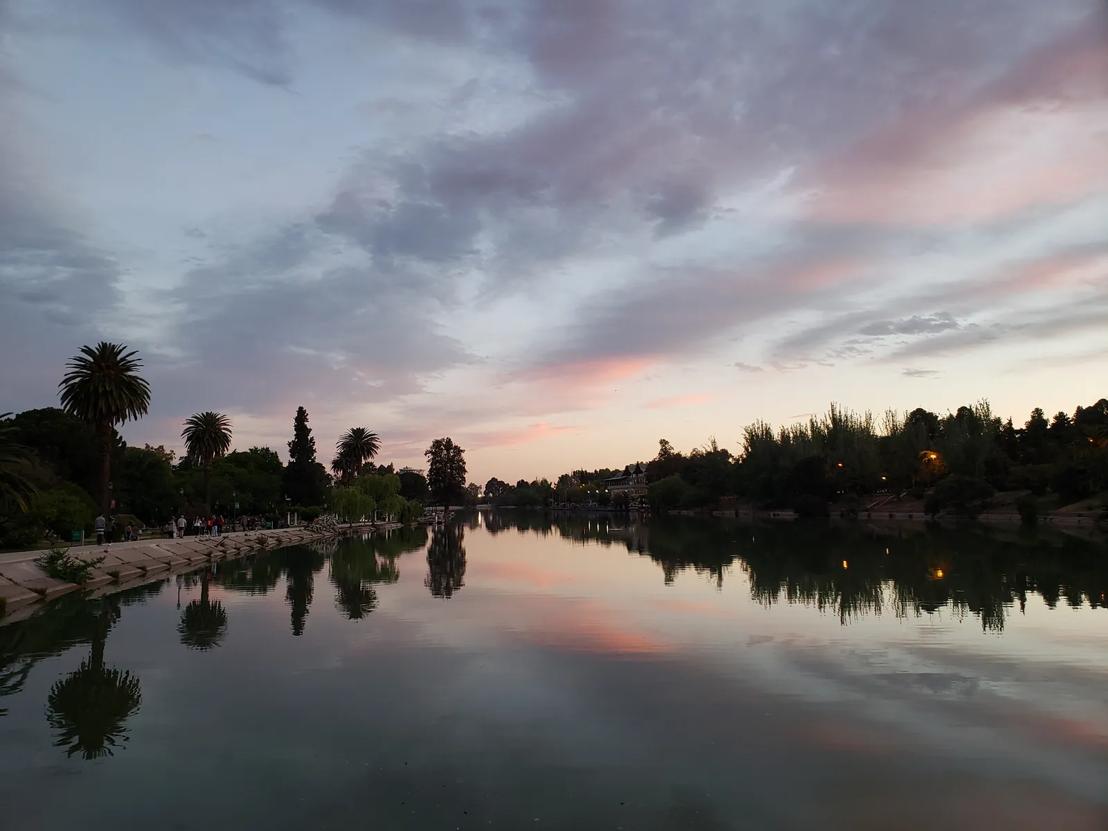 Lago do Parque General San Martín, em Mendoza, refletindo árvores e o céu ao entardecer.
