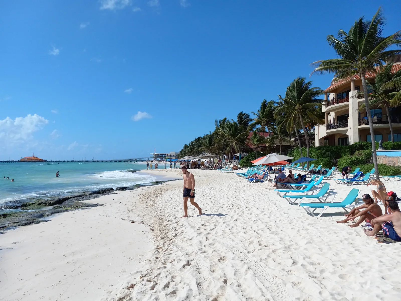 Praia de Playa del Carmen com areia clara, mar azul, coqueiros e espreguiçadeiras na Riviera Maya.
