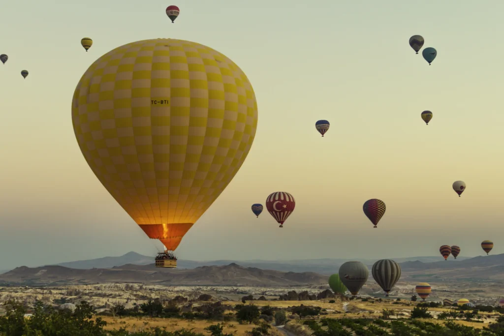 Balões de ar quente sobre a paisagem de Göreme ao amanhecer, na Capadócia, com um balão amarelo em primeiro plano.