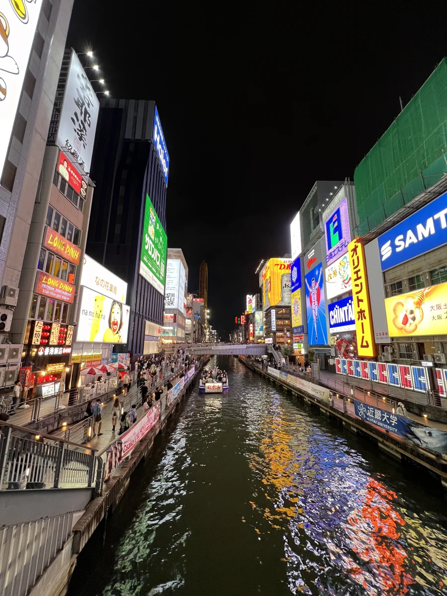 Canal de Dotonbori à noite, com letreiros iluminados e pedestres nas margens, em Osaka.